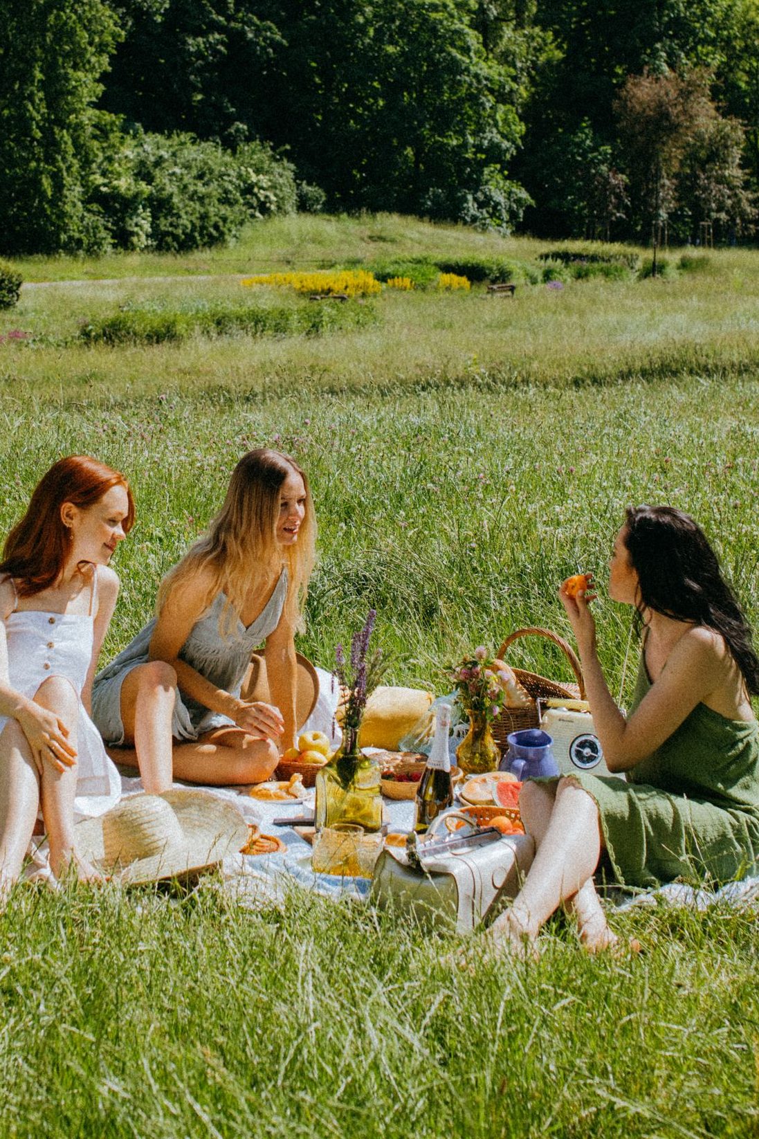 Three women enjoying a relaxed picnic in a sunny park, embracing nature and leisure.